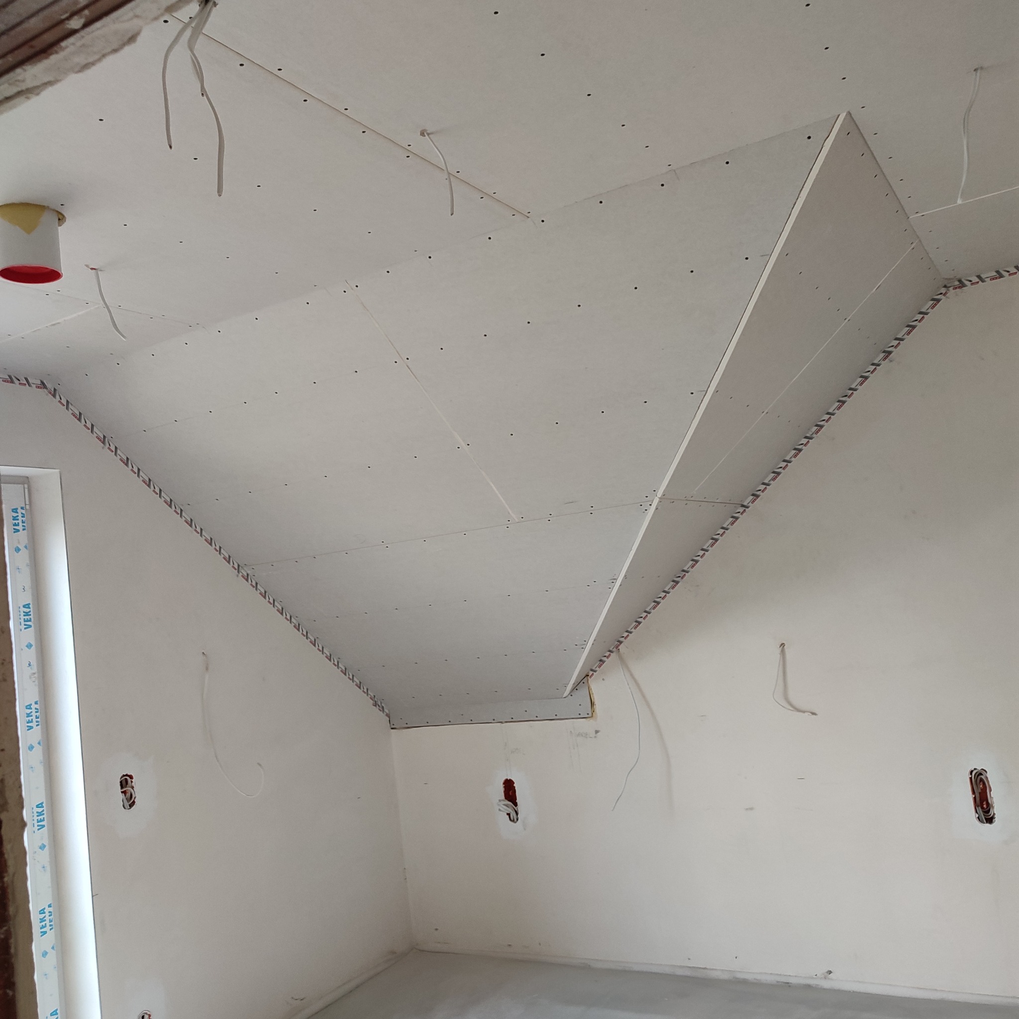 Montaż sufitu podwieszanego z płyt gipsowo-kartonowych w pokoju, widoczne profile przy ścianach i wystające przewody elektryczne.