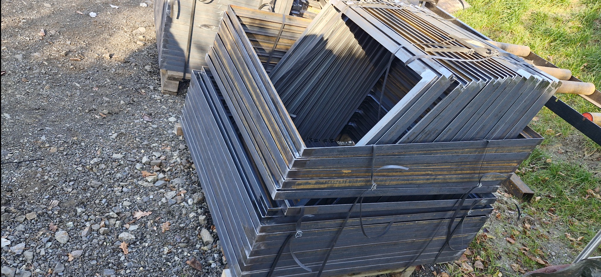 Stos metalowych, surowych elementów konstrukcyjnych, prawdopodobnie do bramy, zabezpieczonych taśmą, na żwirowym podłożu w Domecko. Widok z góry.