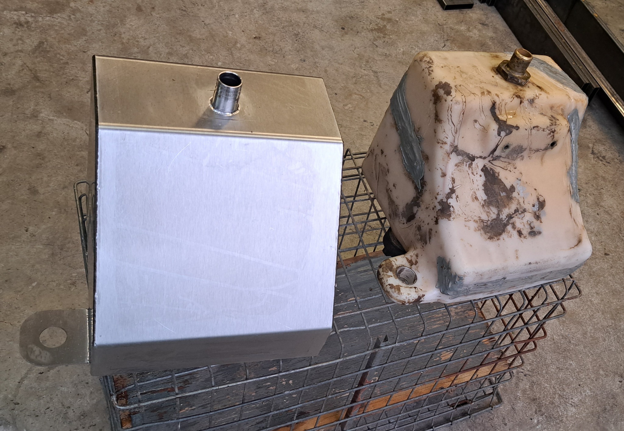 Porównanie: nowy, spawany zbiornik metalowy obok starego, zużytego. Widoczne spawy i mocowanie. Metalowa siatka w tle. Detaliczna prezentacja obróbki metalu.