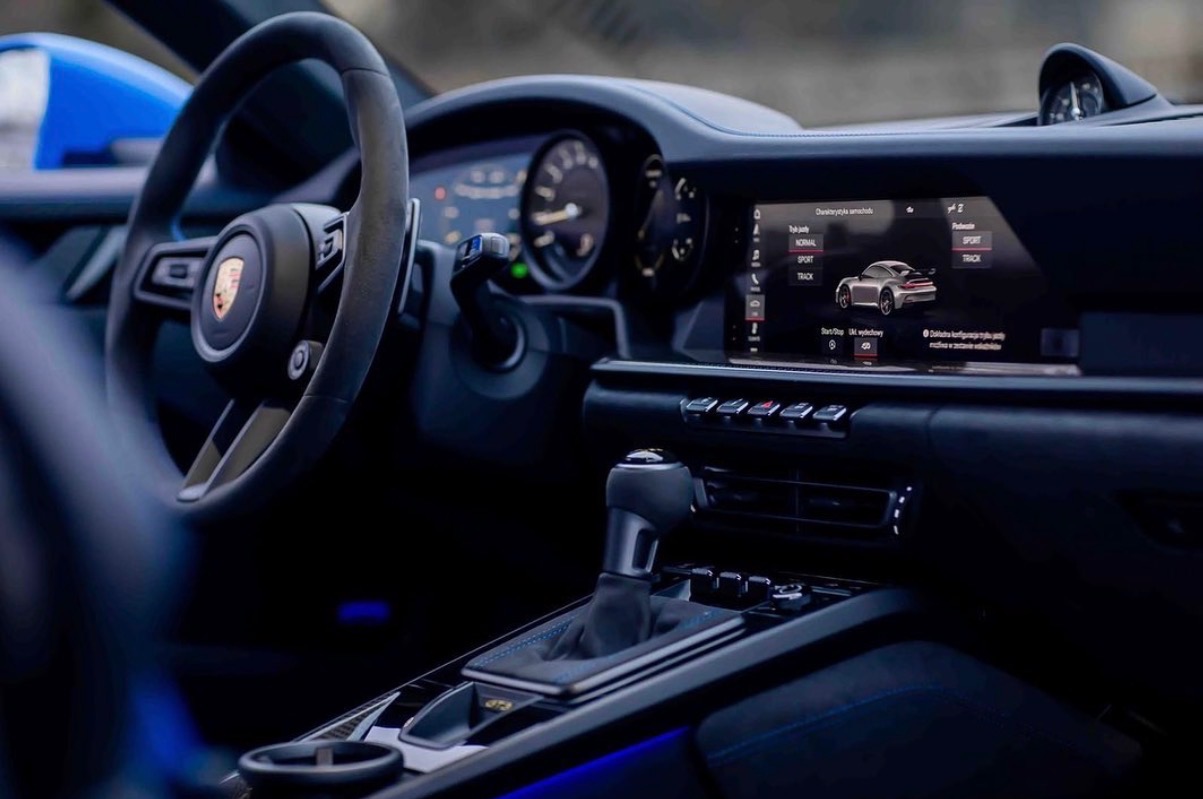 Wnętrze sportowego samochodu Porsche GT3 z widocznym kokpitem, kierownicą, wyświetlaczem i dźwignią zmiany biegów. Detale wykończenia w kolorze niebieskim.