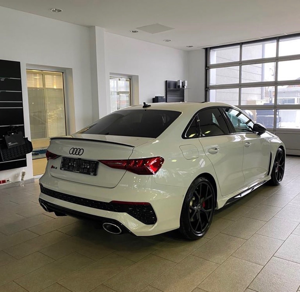 Białe Audi RS3 po detailingu w salonie, widok z tyłu, czarne felgi, światła LED, sportowy dyfuzor, garaż z bramą segmentową w tle.
