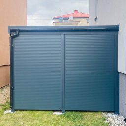 CARGO CENTER SPÓŁKA Z OGRANICZONĄ ODPOWIEDZIALNOŚCIĄ - Nowoczesna, grafitowa zabudowa balkonu z poziomymi panelami, widoczna z zewnątrz, z fragmentami elewacji domu po bokach i trawnikiem u dołu.