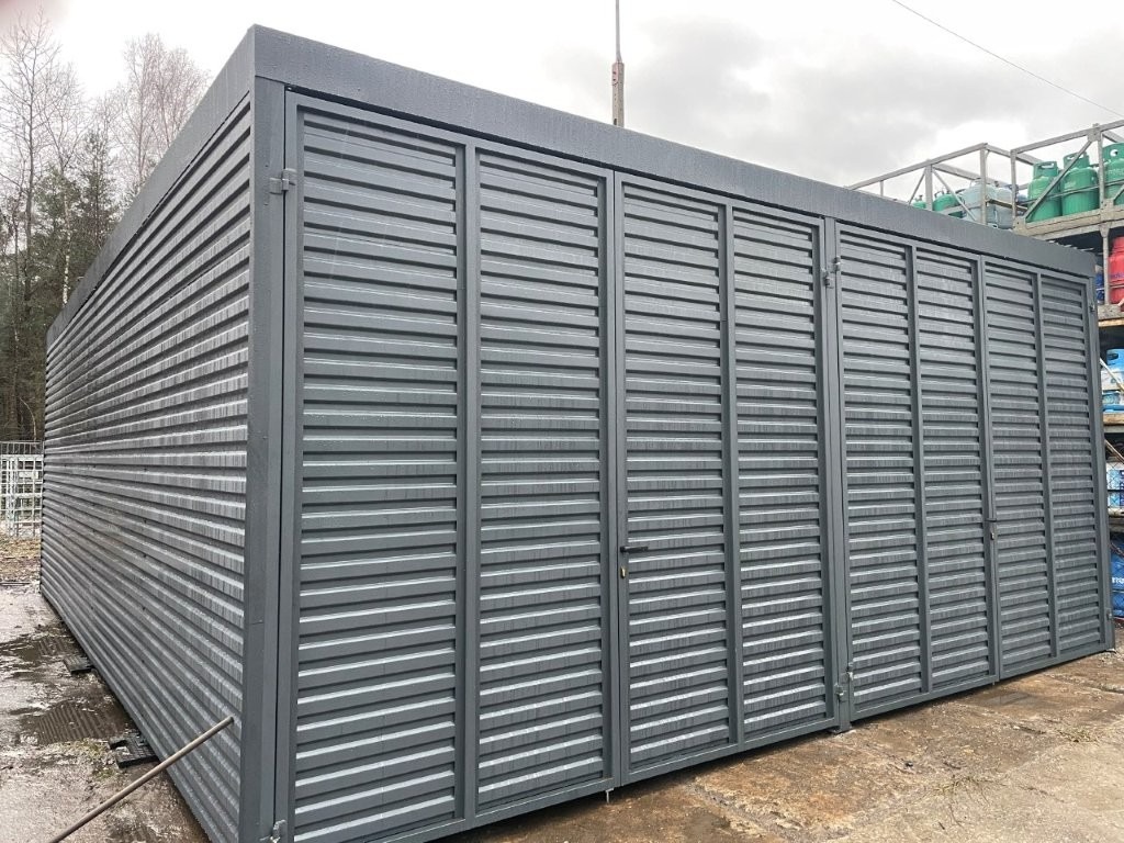 Szara, metalowa konstrukcja z żaluzjowymi panelami, prawdopodobnie zabudowa balkonu lub tarasu, z widocznymi butlami gazowymi w tle.