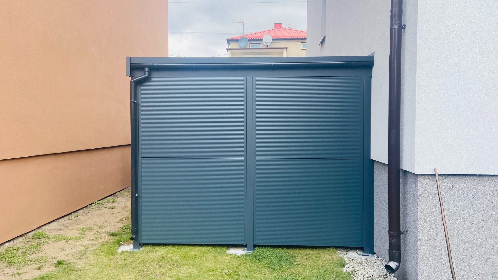 Nowoczesna, grafitowa zabudowa balkonu z poziomymi panelami, widoczna z zewnątrz, z fragmentami elewacji domu po bokach i trawnikiem u dołu.