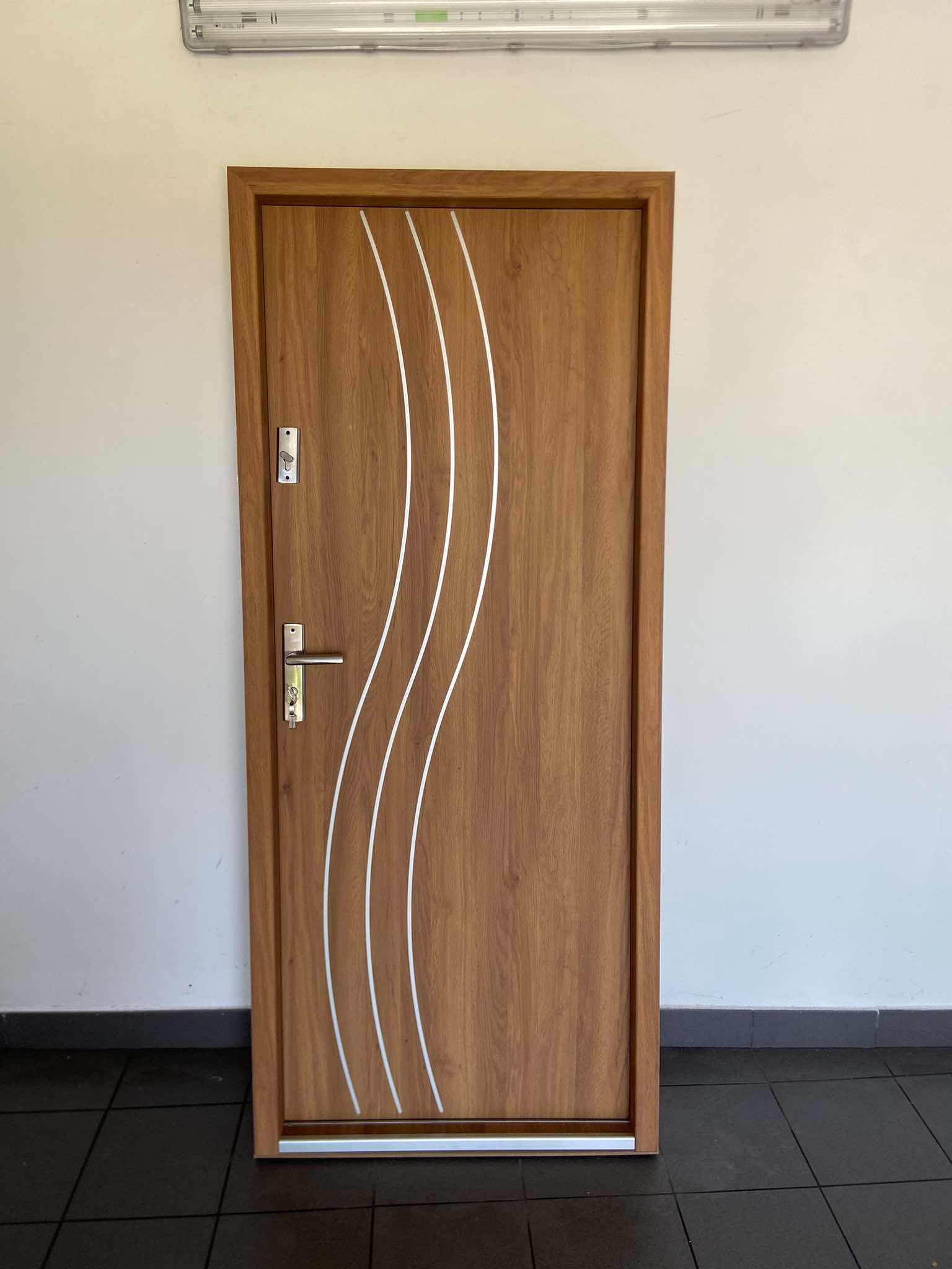 Brązowe drzwi z trzema białymi, falistymi intarsjami, srebrna klamka i zamek, na tle białej ściany i ciemnej podłogi.