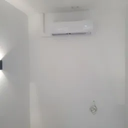 Biały klimatyzator ścienny z wyświetlaczem temperatury (17 stopni Celsjusza) zamontowany w minimalistycznym wnętrzu z widocznymi przewodami.