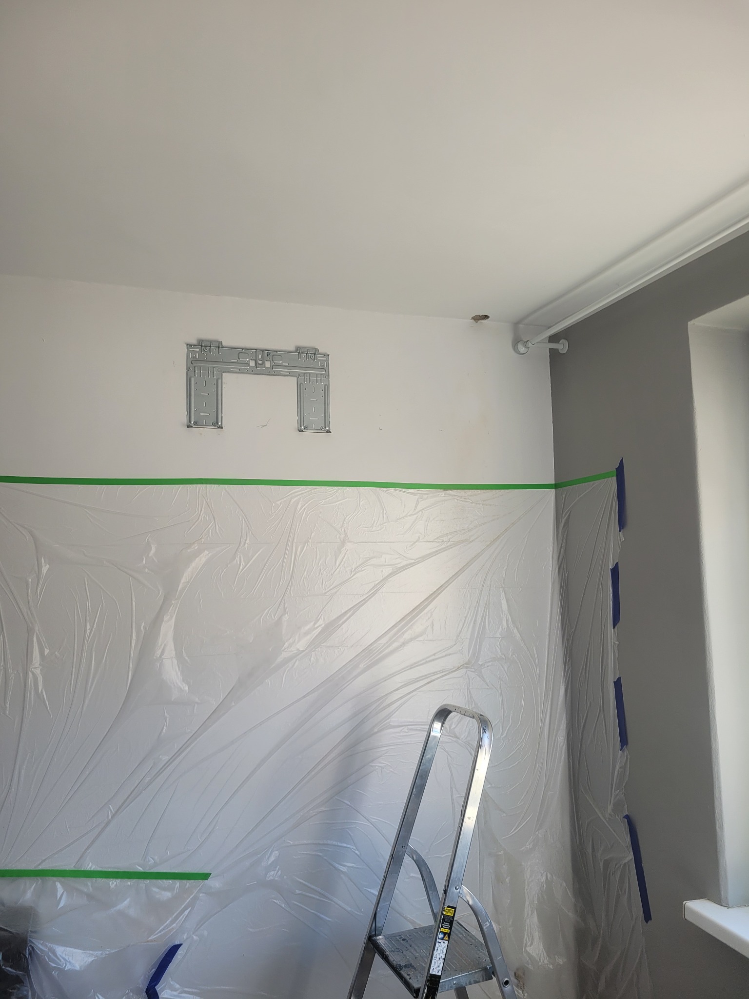 Przygotowanie do montażu klimatyzacji w pomieszczeniu: zamontowany stelaż na ścianie, zabezpieczenie folią malarską, drabina aluminiowa.