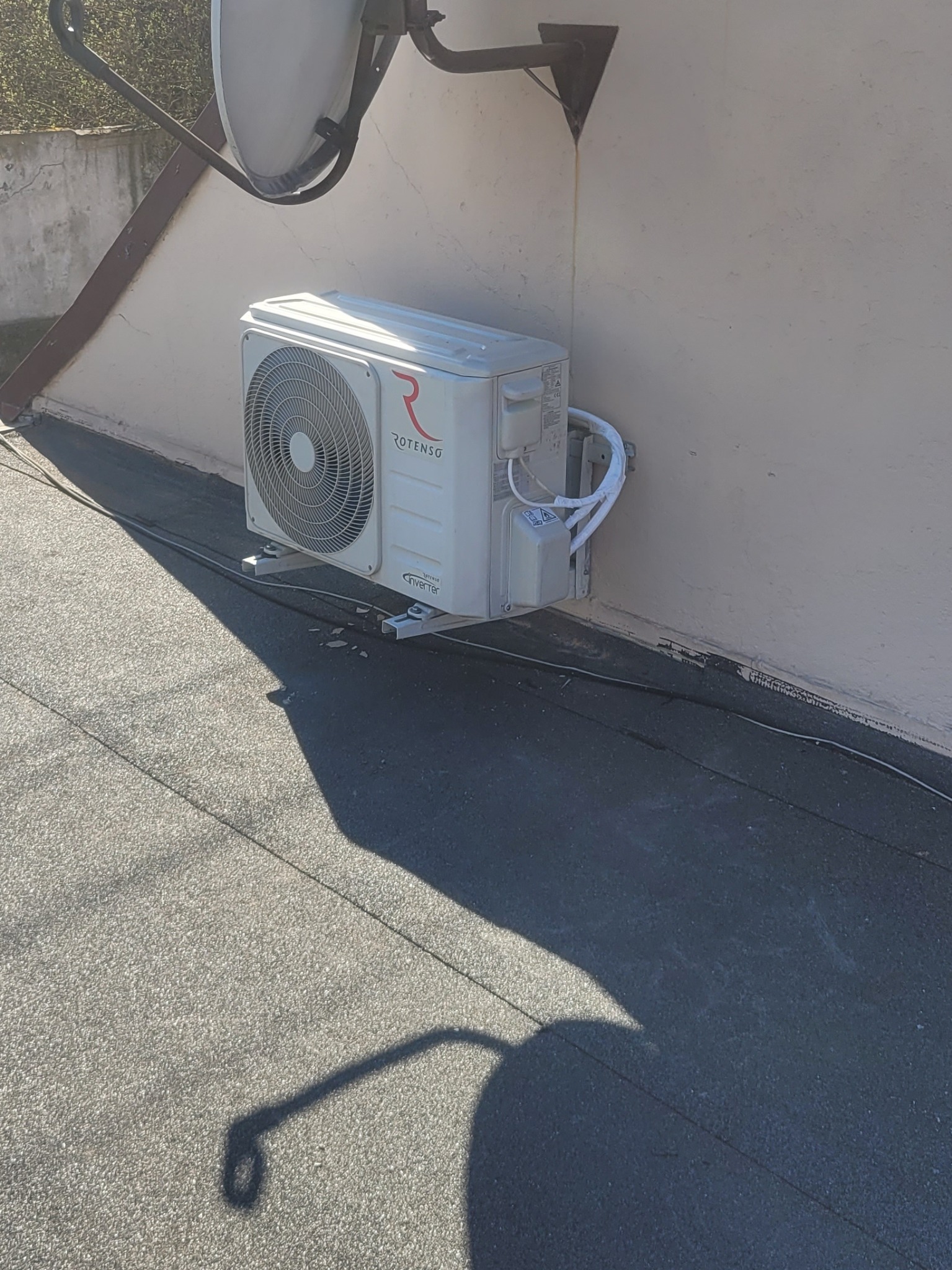 Zewnętrzna jednostka klimatyzacji Rotenso zamontowana na ścianie budynku w Rawiczu, widoczne przewody i cień anteny satelitarnej.