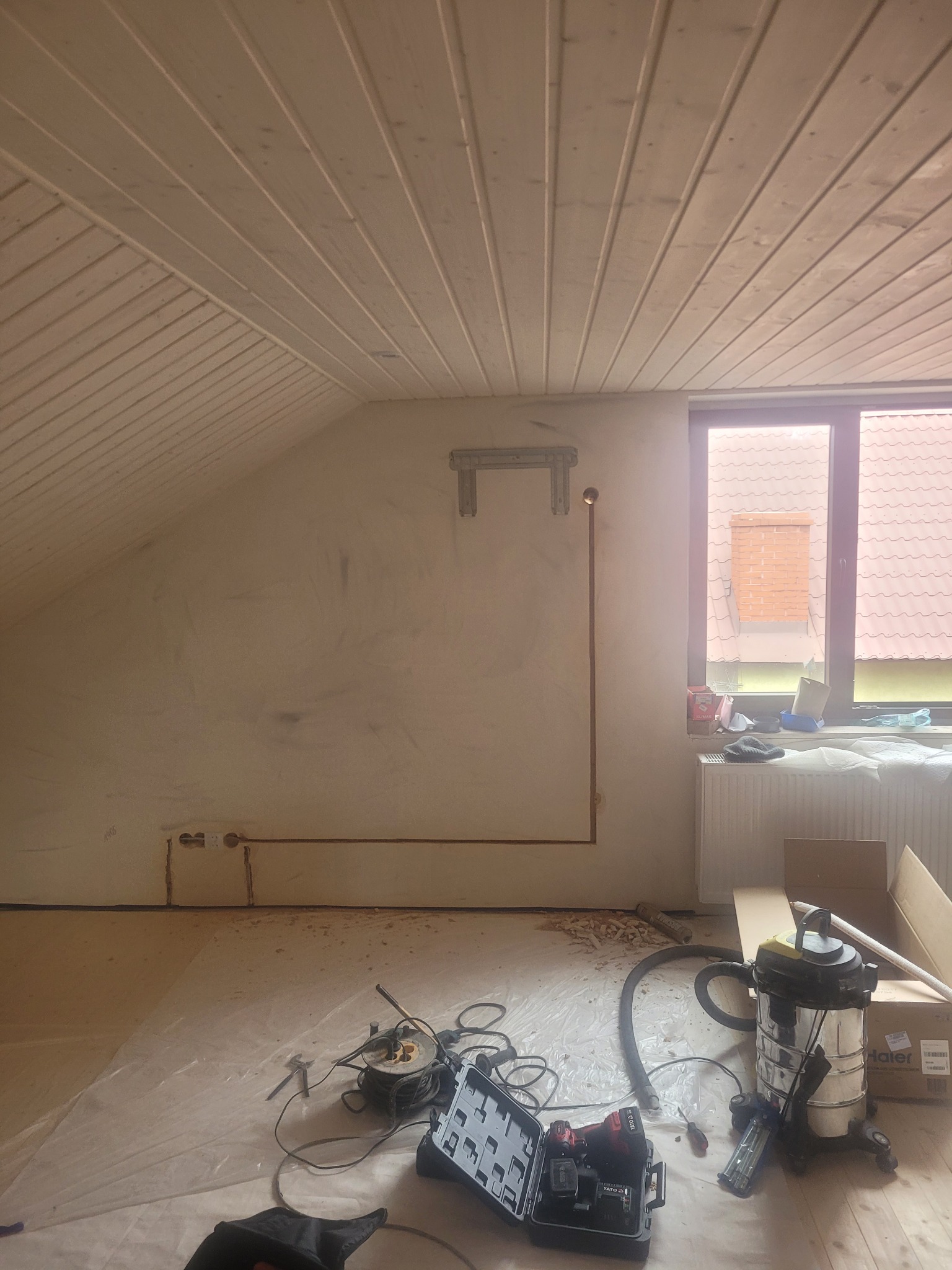 Montaż instalacji klimatyzacji na poddaszu: widoczne rury miedziane, uchwyt ścienny, narzędzia i odkurzacz przemysłowy. Ściany przygotowane do dalszych prac wykończeniowych.