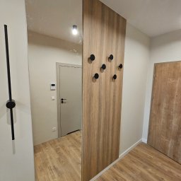 hm-meble marcin heinrich - Wnętrze przedpokoju z dużą szafą z lustrem i drewnianym panelem z czarnymi, okrągłymi wieszakami, odbicie podłogi w lustrze, drzwi w tle.