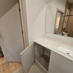 hm-meble marcin heinrich - Nowoczesna łazienka z szafką pod umywalką o otwartych drzwiczkach, widoczne przyłącza elektryczne nad blatem, odbicie wnętrza w lustrze.