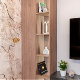 Wysoka, drewniana szafa wnękowa z p&oacute;łkami, na kt&oacute;rych stoją książki i dekoracyjne wazony, obok telewizora i rośliny doniczkowej.