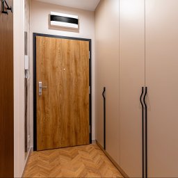 hm-meble marcin heinrich - Nowoczesny przedpokój z jasnymi drzwiami wejściowymi, beżowymi zabudowami z czarnymi, falistymi uchwytami i drewnianą podłogą w jodełkę.