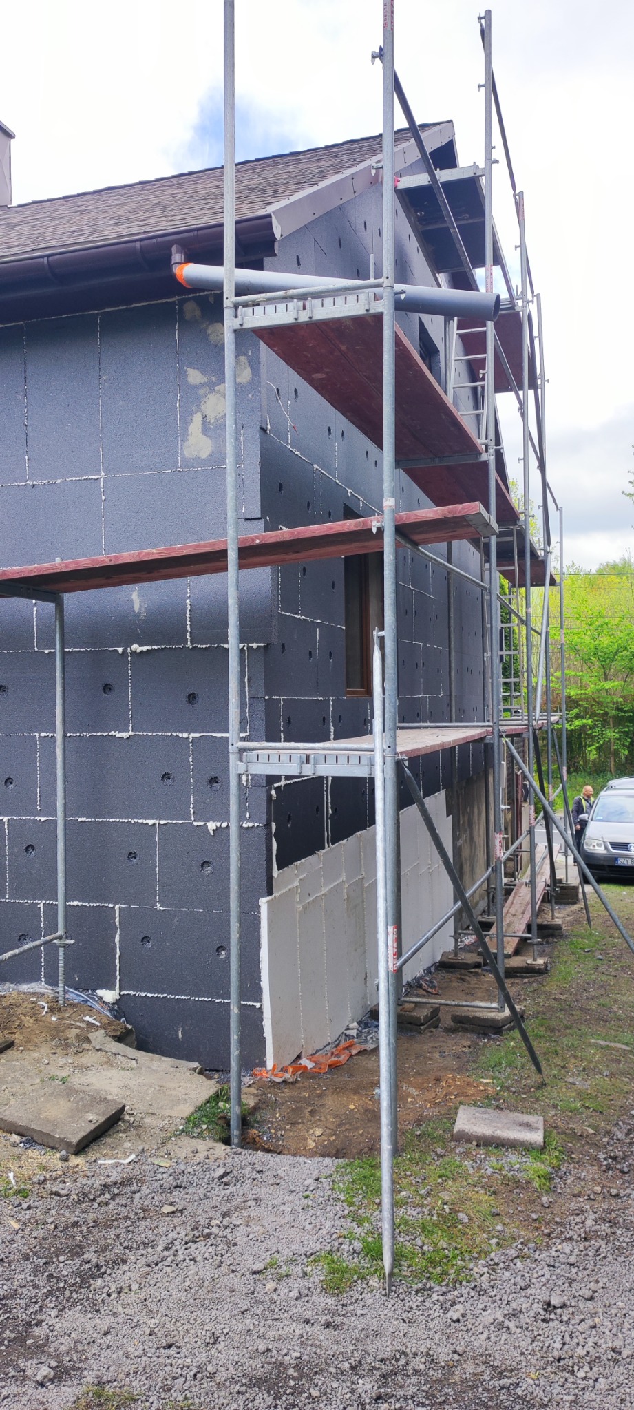Ocieplanie elewacji domu jednorodzinnego z użyciem styropianu grafitowego, widoczne rusztowanie i częściowo położona warstwa izolacyjna na ścianie szczytowej.