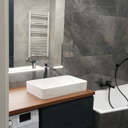 Usługi remontowo-budowlane Rafał Brzóska - Nowoczesna łazienka z umywalką nablatową, baterią w kolorze czarnym, podświetlanym lustrem, grzejnikiem drabinkowym i pralką w zabudowie.
