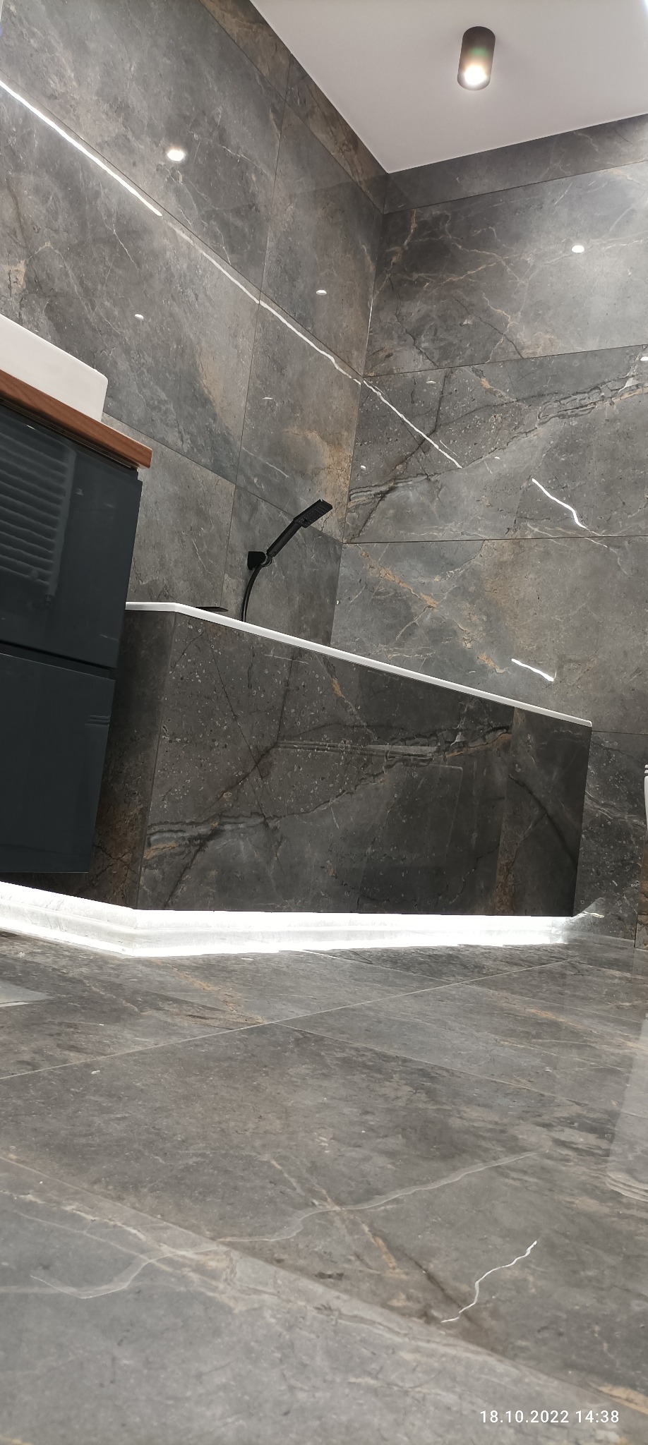 Nowoczesna łazienka z szarymi płytkami imitującymi marmur, podświetlana wanna i czarna armatura, widok z niskiego kąta.