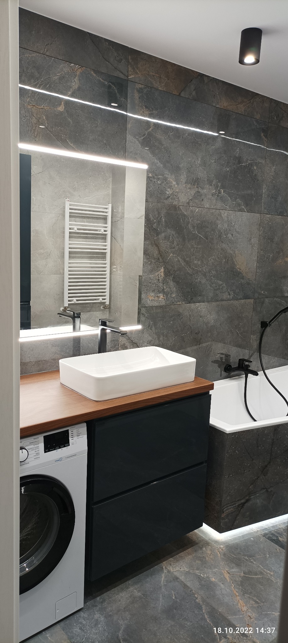 Nowoczesna łazienka z umywalką nablatową, baterią w kolorze czarnym, podświetlanym lustrem, grzejnikiem drabinkowym i pralką w zabudowie.