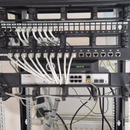 Kranikontakt - Szafa rackowa z uporządkowaną instalacją sieciową: białe patch cordy Cat.6 wpięte w patch panele z etykietami K1-K10 oraz switchem Tiandy Gigabit PoE.