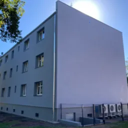 Odnowiona elewacja bloku mieszkalnego w odcieniach szarości z zainstalowanymi klimatyzatorami, oświetlona jasnym słońcem i błękitnym niebem. Widok z dołu.