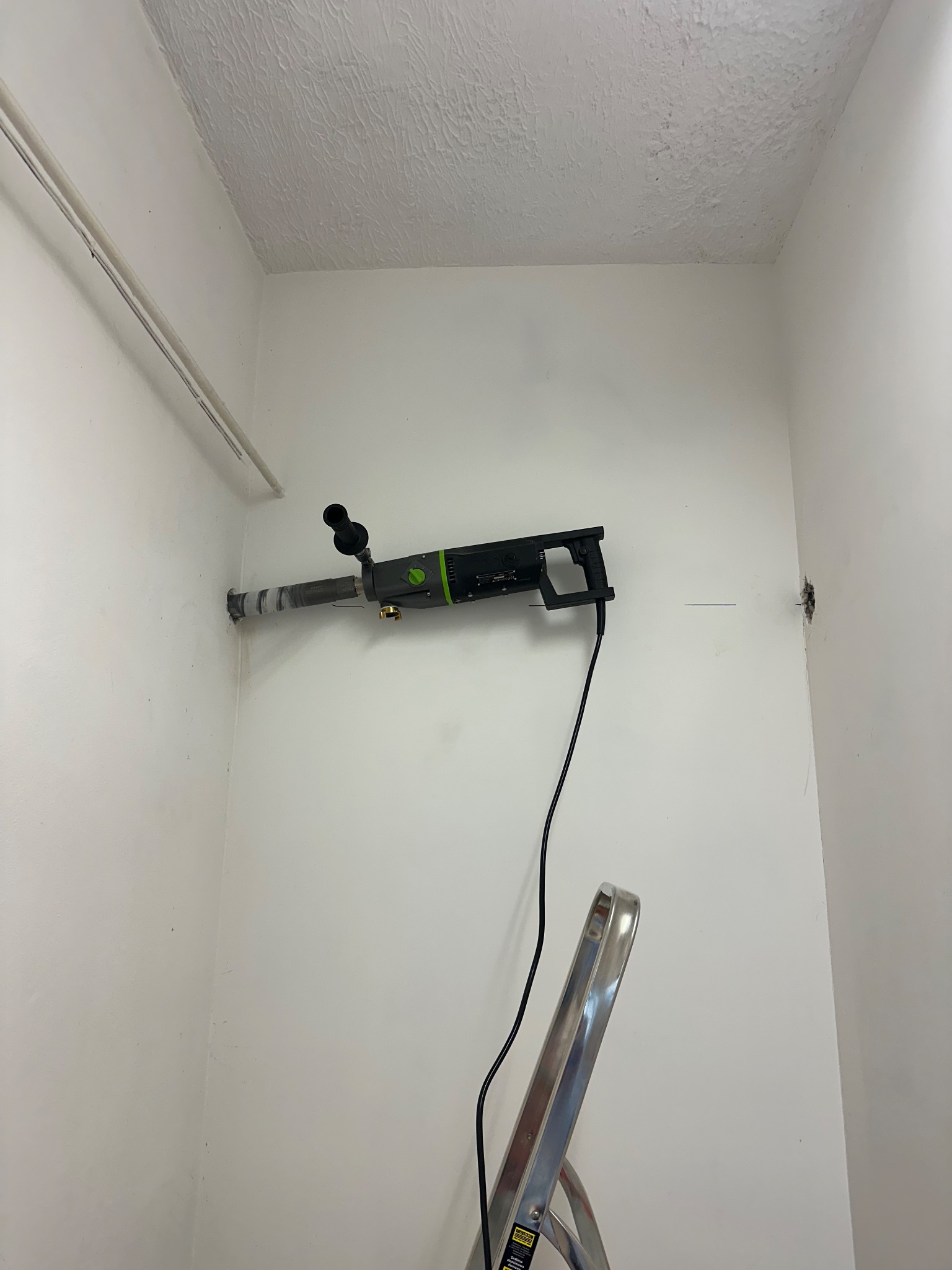 Wiercenie otworu pod klimatyzację w Gdańsku. Wiertło w ścianie, drabina. Praca instalatora klimatyzacji w pomieszczeniu o białych ścianach i surowym wykończeniu.