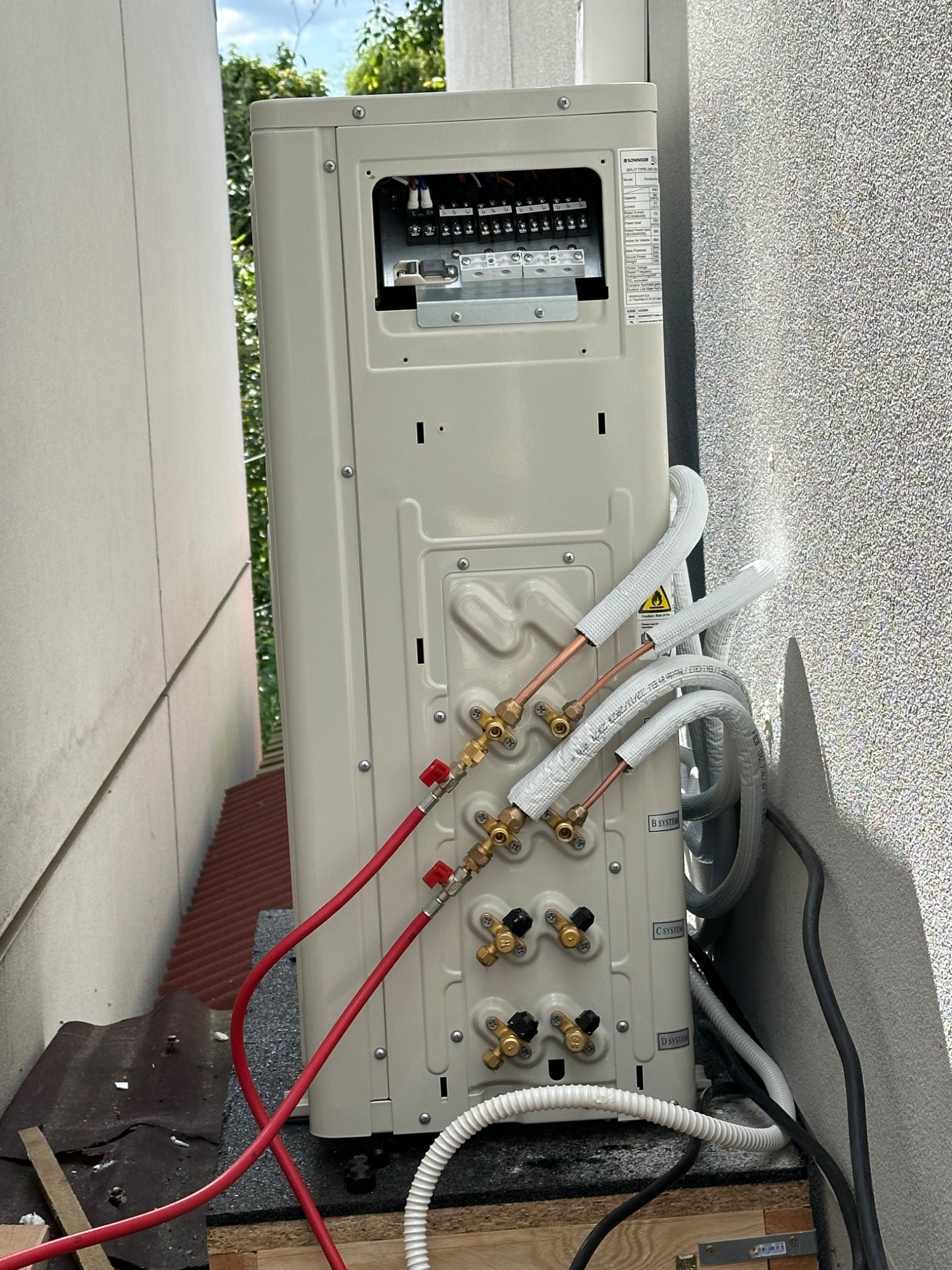 Montaż klimatyzacji: tylny panel jednostki zewnętrznej z podłączonymi rurami miedzianymi i przewodami, widok z bliska na instalację w przestrzeni między budynkami.