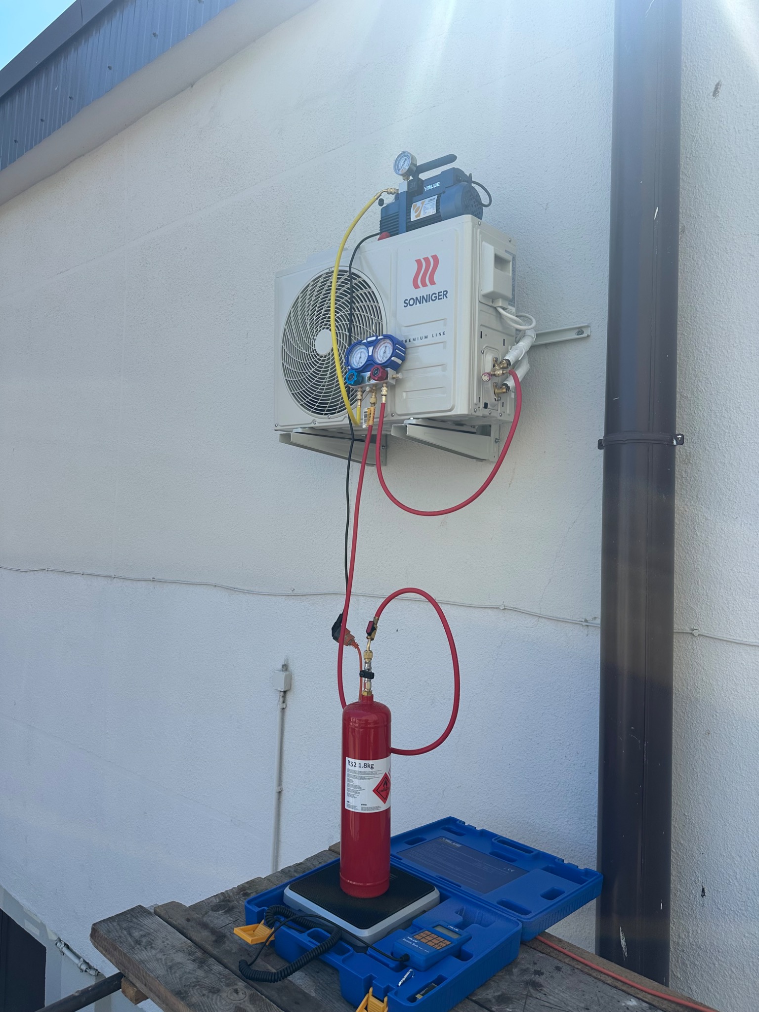 Montaż klimatyzacji SONNIGER na elewacji budynku. Widoczne narzędzia: butla z czynnikiem chłodniczym R32, waga, manometry. Instalacja w trakcie podłączenia.