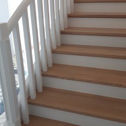 ART-DREW USŁUGI STOLARSKIE NIP 777 177 04 26 - Drewniane schody z białymi balustradami i podstopnicami, widok z dołu. Naturalne oświetlenie podkreśla teksturę drewna.