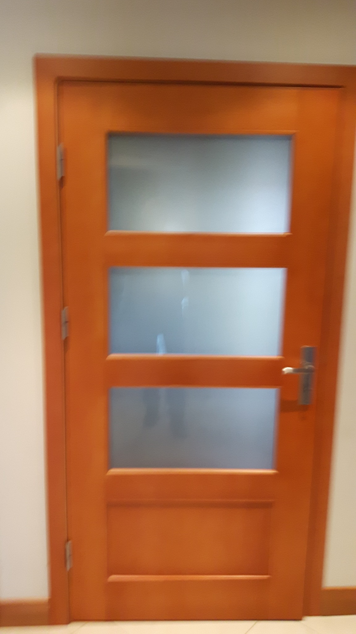 Drewniane drzwi wewnętrzne z trzema szybami matowymi, wykończone w ciepłym odcieniu brązu. Realizacja w Stęszewie. Minimalistyczny design.