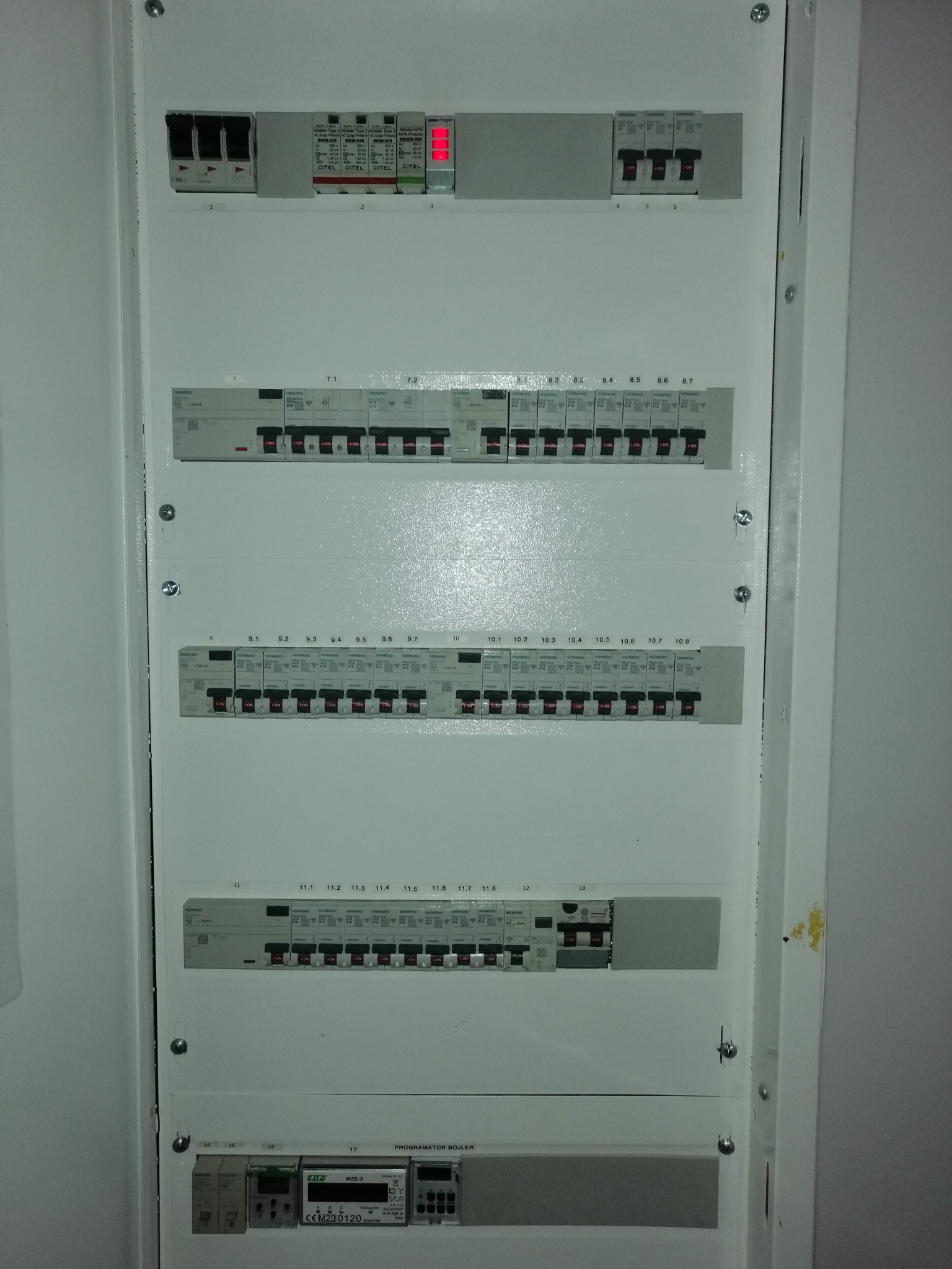 Rozdzielnica elektryczna z zabezpieczeniami różnicowoprądowymi i nadprądowymi, widoczne bezpieczniki firmy Siemens oraz programator bojlera.