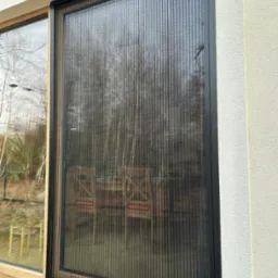 Zewnętrzna moskitiera plisowana z czarną ramą, widok z bliska na okno z widokiem na ogród.