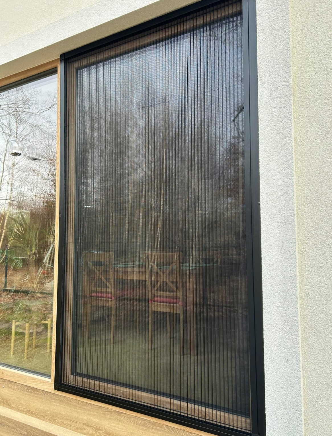 Zewnętrzna moskitiera plisowana z czarną ramą, widok z bliska na okno z widokiem na ogród.