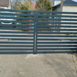 Nowoczesna, pozioma brama dwuskrzydłowa w kolorze grafitowym z zamontowaną automatyką, na pierwszym planie wkrętarka akumulatorowa