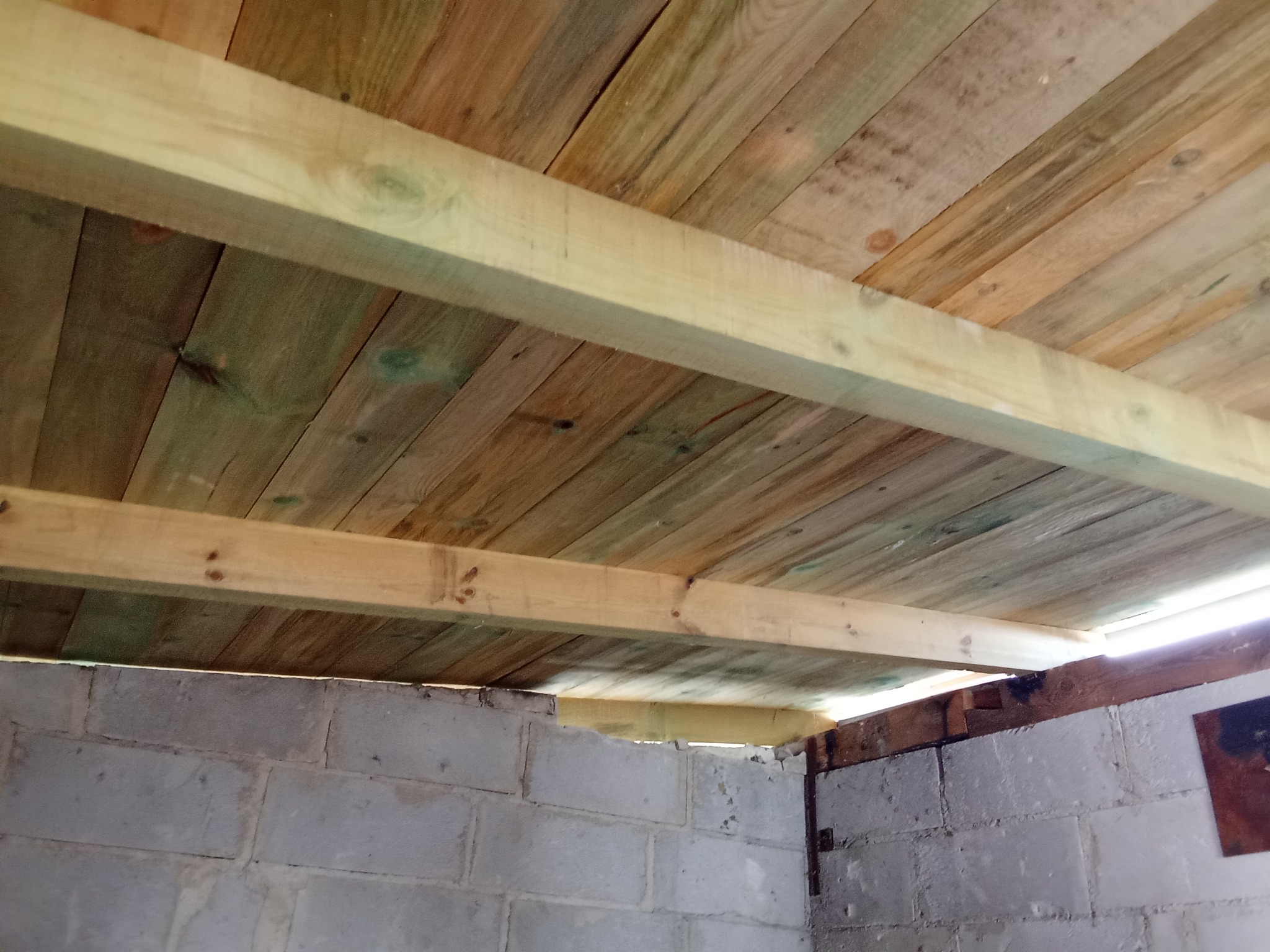 Konstrukcja drewnianego stropu nad murowaną ścianą z bloczków betonowych, widoczne deski i belki nośne, surowy stan wykończenia.