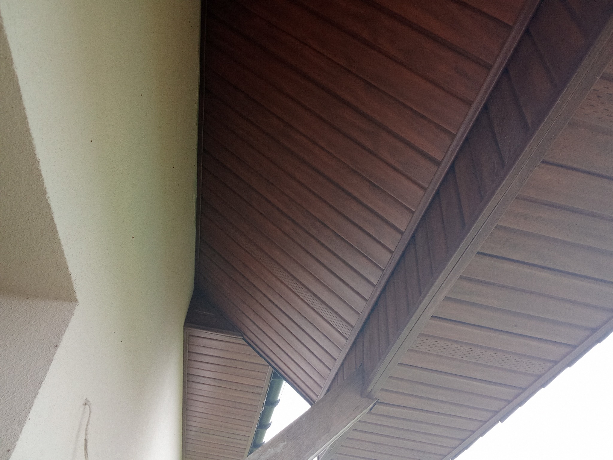 Podbitka dachowa z brązowego panela PCV zamontowana pod okapem, widok z dołu na fragment elewacji budynku.