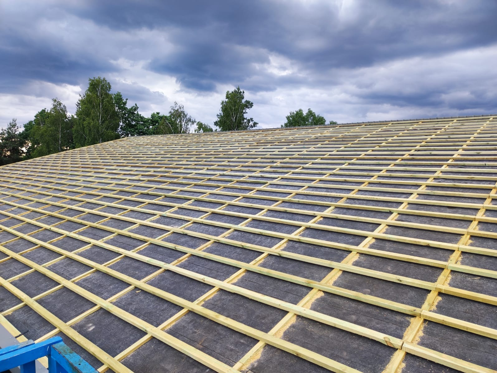 Przygotowany podkład z papy i drewnianych łat pod nowe pokrycie dachowe, widok z góry, pochmurne niebo w tle.