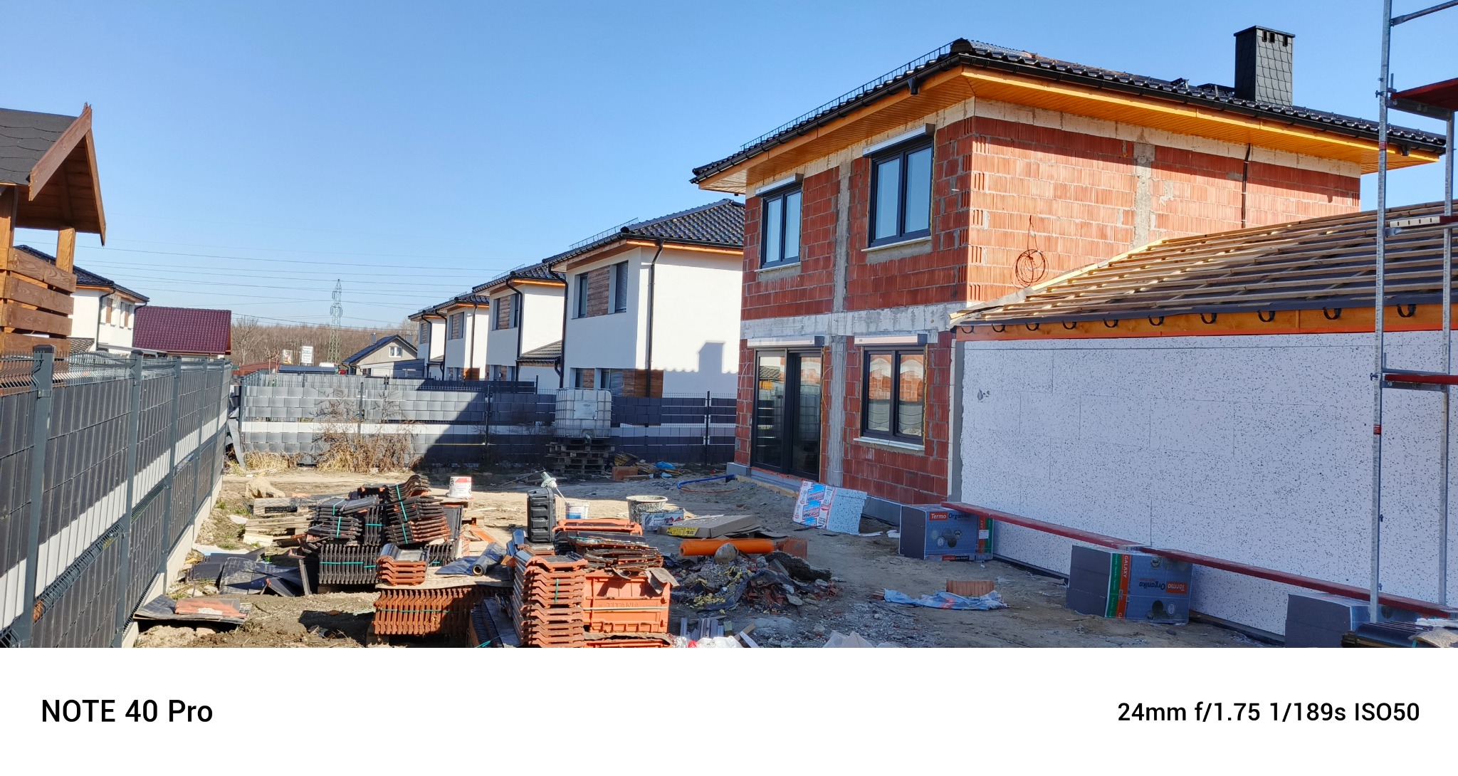 Budowa domu jednorodzinnego w trakcie ocieplania elewacji. Widoczne bloczki ceramiczne, styropian, rusztowanie. Częściowo ocieplony budynek w słoneczny dzień.