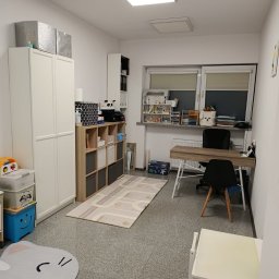 SzumiMi Praktyka Logopedyczno-Pedagogiczna Magdalena Nowakowska - Pokój terapeutyczny z biurkiem, regałami i dywanem z motywem ulicy. Stonowana kolorystyka, jasne oświetlenie, przytulna aranżacja przestrzeni dla dzieci.