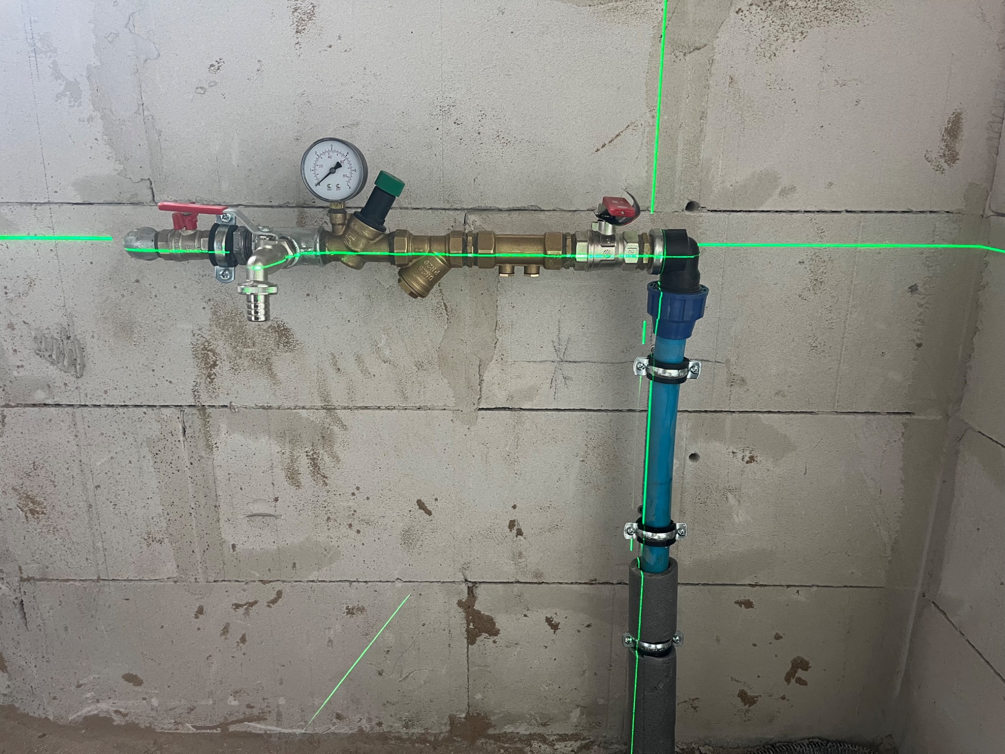 Instalacja wodna z manometrem i filtrem, rury z niebieskiego tworzywa z izolacją, poziomowanie laserowe na surowej ścianie z betonu komórkowego.