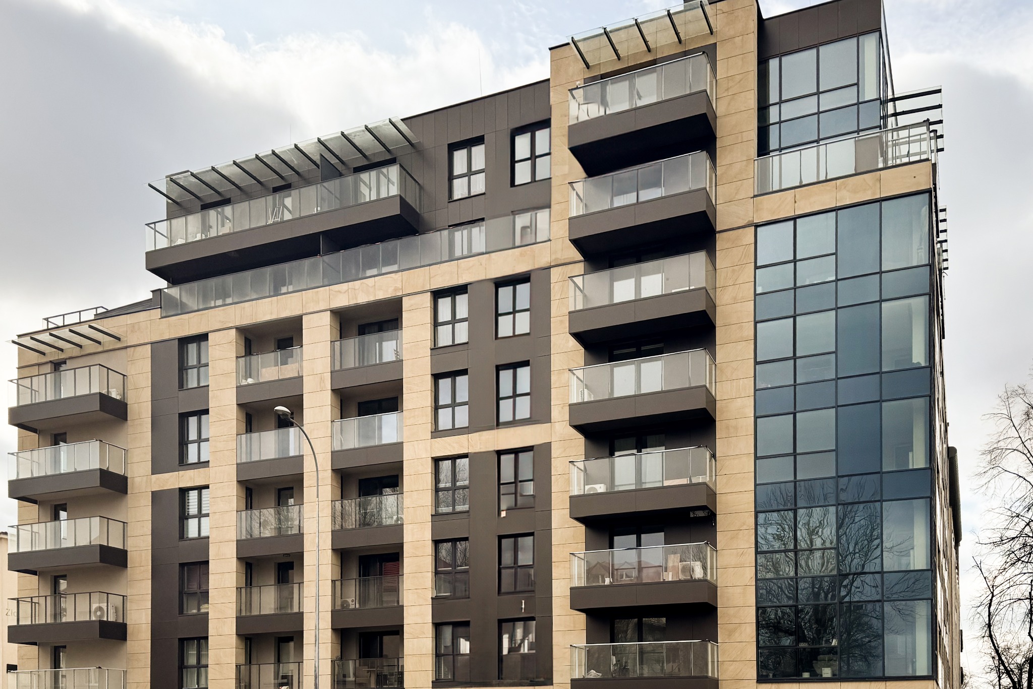 Nowoczesny budynek biurowo-mieszkalny z balkonami i przeszkloną fasadą, widok z dołu na błękitne niebo.