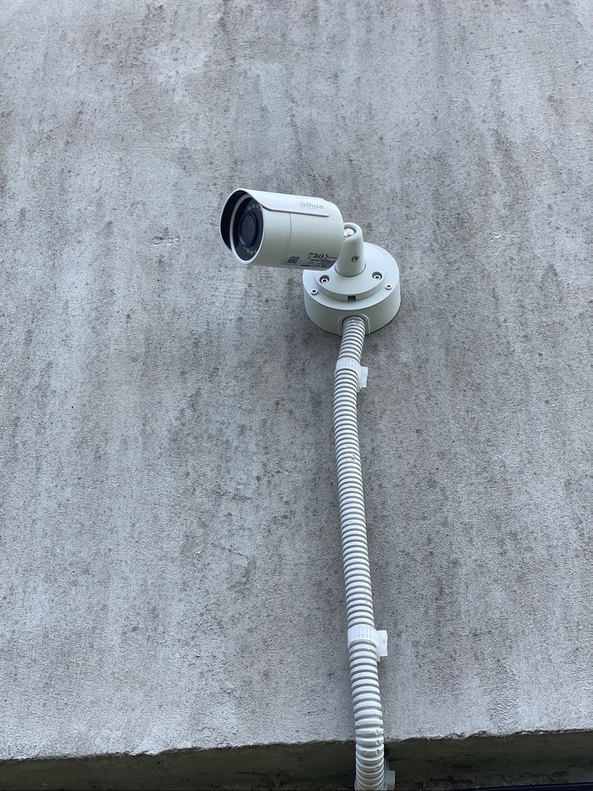 Zamontowana kamera monitoringu Dahua na szarej, chropowatej ścianie z widoczną rurą osłonową kabla.