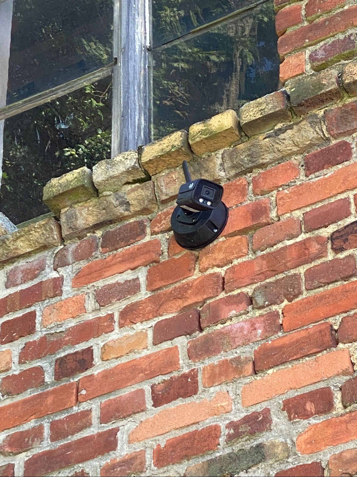 Zewnętrzna kamera monitoringu zamontowana na ceglanej ścianie budynku obok okna.