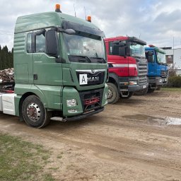 ADPOL Leszek Zarembski - Trzy ciężarówki różnych marek (MAN, Scania, Mercedes) zaparkowane na błotnistym terenie, z zieloną ciężarówką MAN z załadowanym drewnem z tyłu.