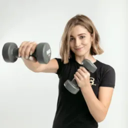 Uśmiechnięta kobieta z krótkimi blond włosami, w czarnej koszulce z logo, trzyma dwie szare hantle na białym tle.