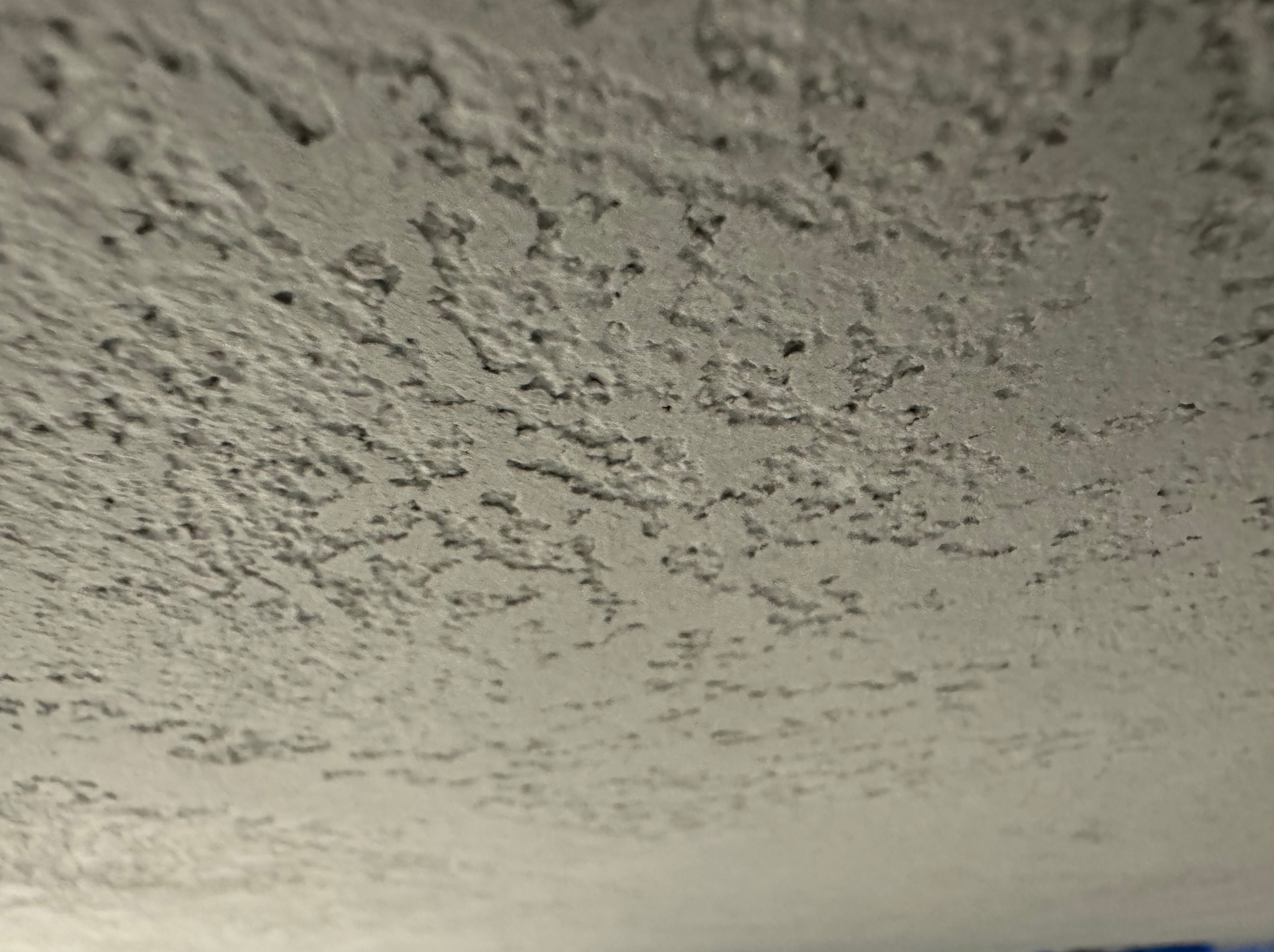 Szara, nierówna faktura ściany z bliska, przypominająca tynk strukturalny z licznymi wgłębieniami i wypukłościami.