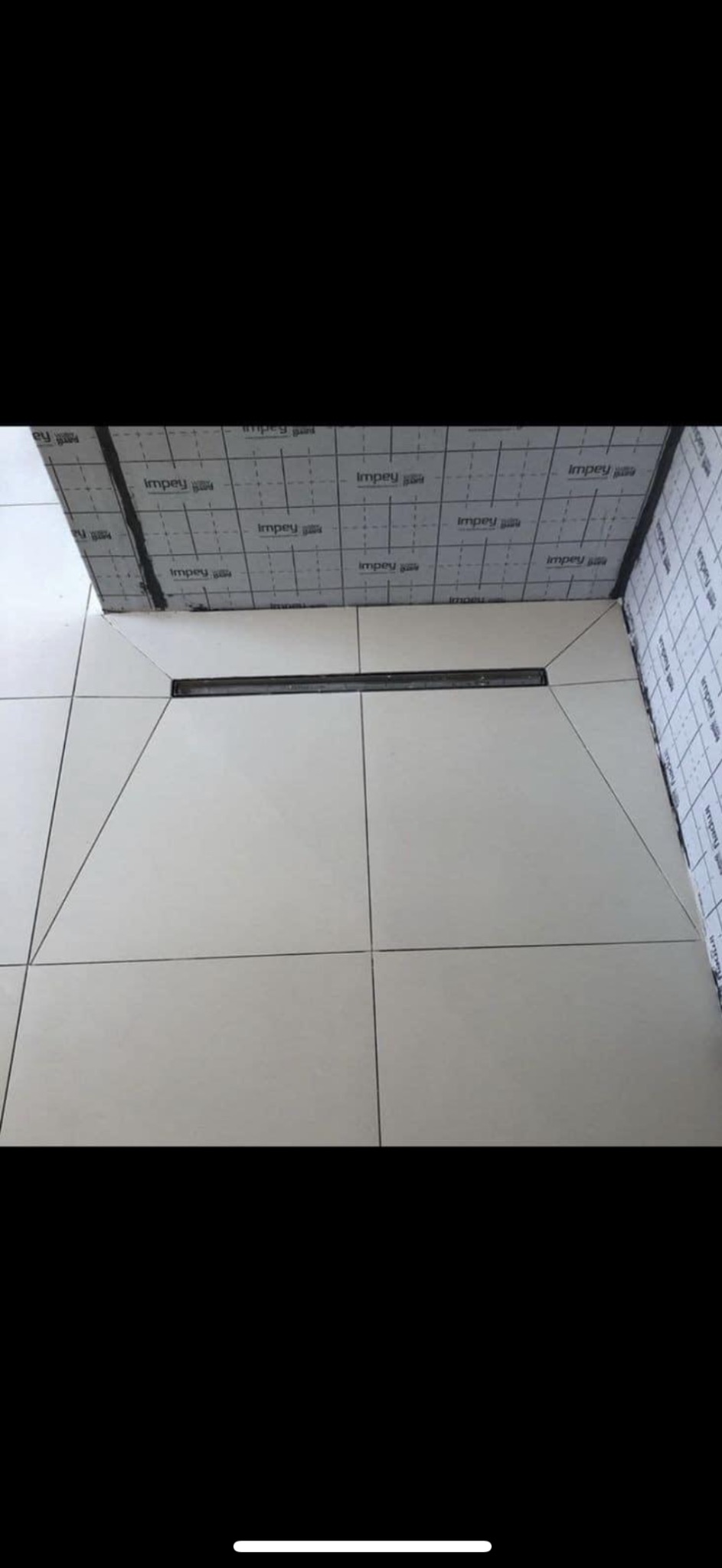 Białe płytki podłogowe w łazience z zamontowanym odpływem liniowym, widoczna izolacja przeciwwodna na ścianach.