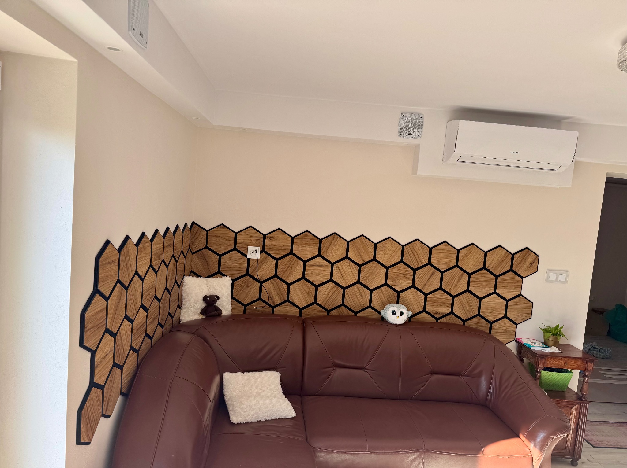 Salon z dekoracyjną ścianą z drewnianych heksagonów, brązową skórzaną sofą i klimatyzatorem na ścianie
