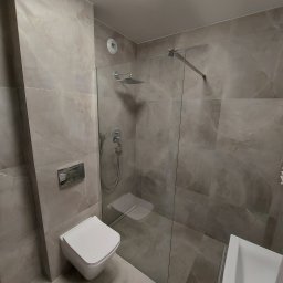 Oleksandr Turchynskyi - Nowoczesna łazienka z szarymi płytkami imitującymi marmur, kabina prysznicowa typu walk-in ze szklaną ścianką, podwieszana toaleta i umywalka nablatowa, oświetlenie sufitowe.