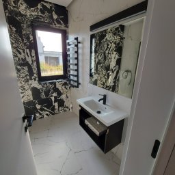 Oleksandr Turchynskyi - Wykończona łazienka we Wrocławiu z czarno-białymi marmurkowymi płytkami na ścianach i podłodze, z czarną armaturą i grzejnikiem drabinkowym oraz oknem z widokiem na budowę.