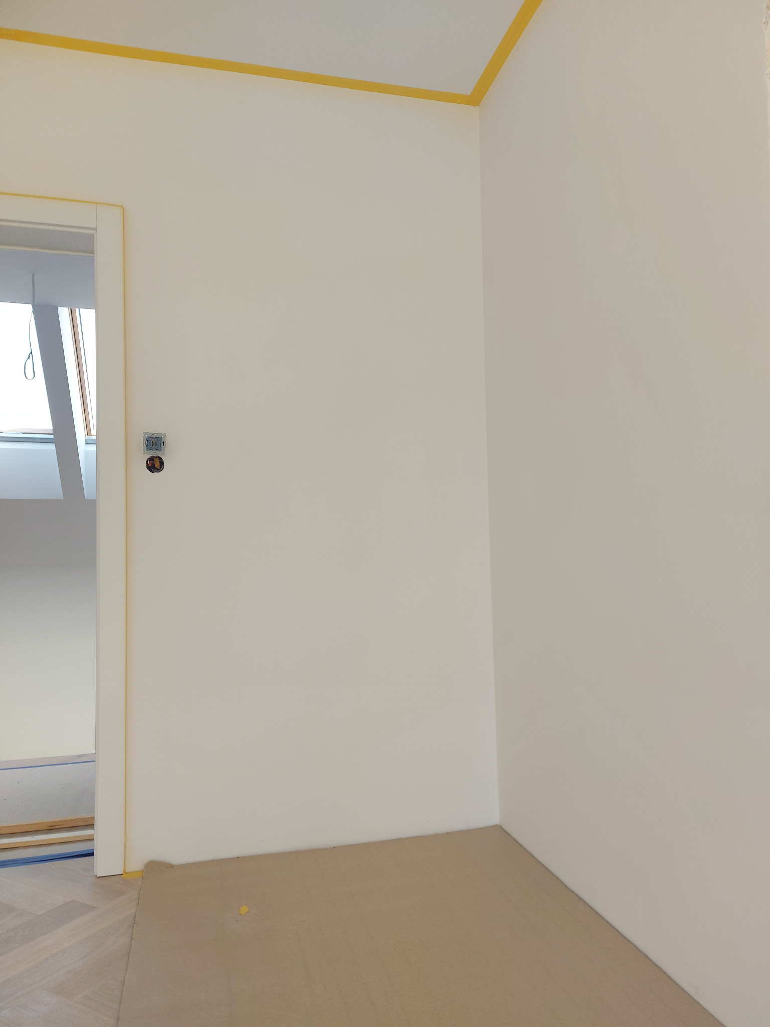 Wnętrze pokoju we Wrocławiu przygotowane do malowania ścian, z zabezpieczoną taśmą żółtą górną krawędzią i folią na podłodze, widoczny fragment podłogi z parkietu oraz otwór drzwiowy z widocznym...