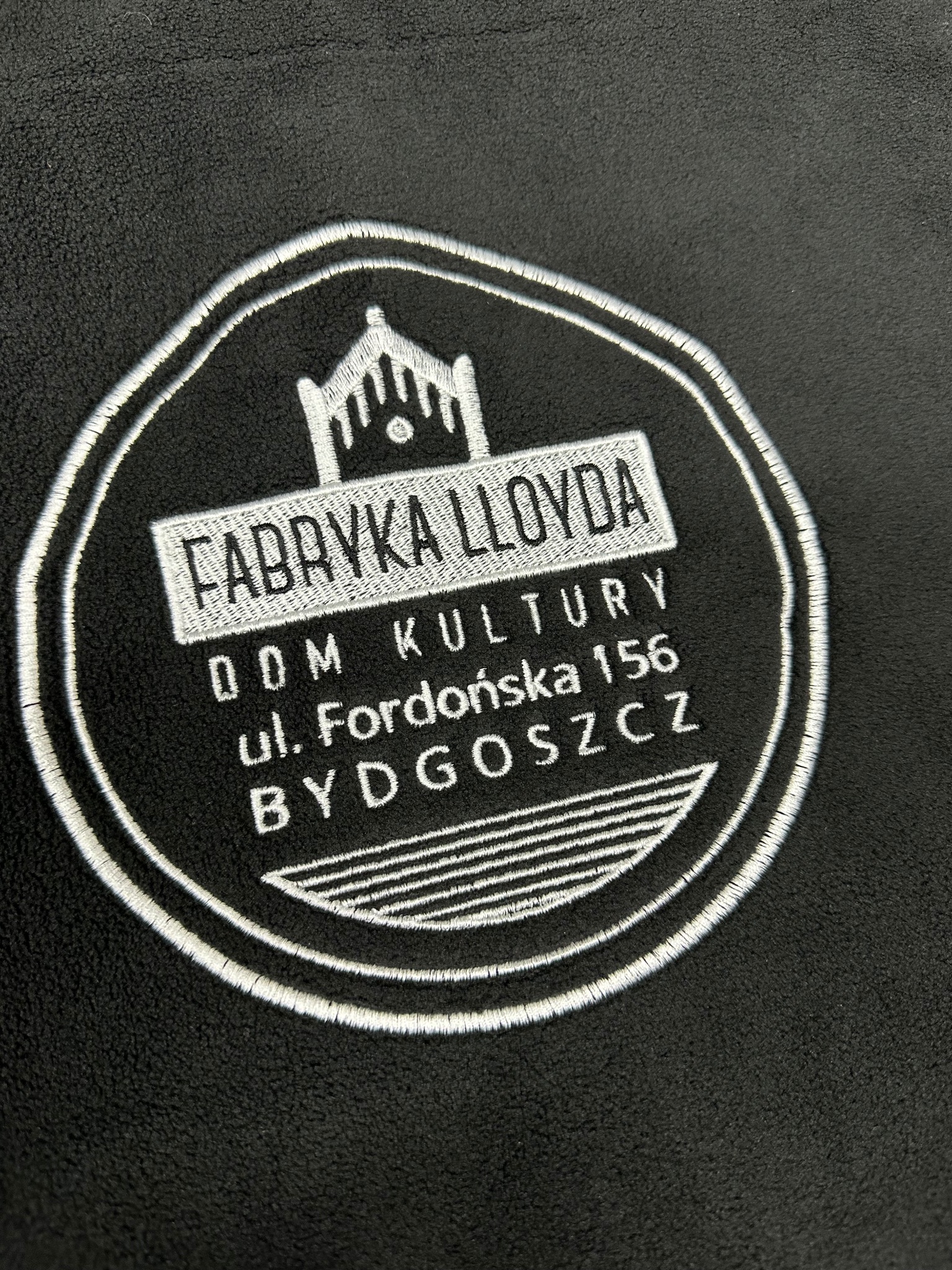 Czarny polar z wyhaftowanym białym logo Fabryki Lloyda, Dom Kultury, ul. Fordońska 156, Bydgoszcz, w okrągłej ramce.